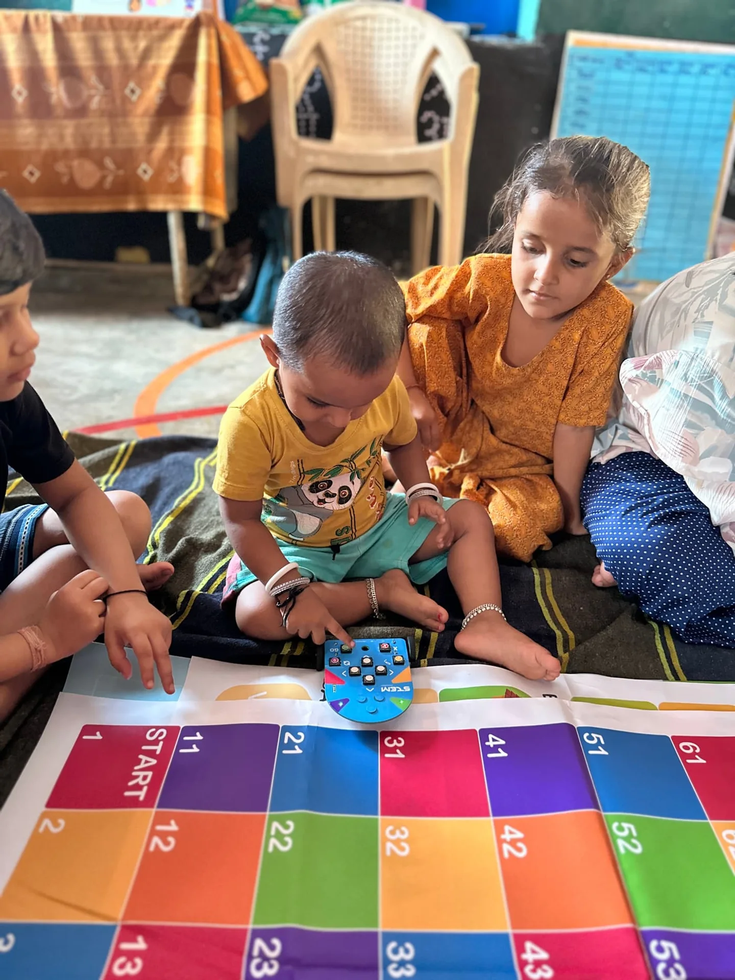 Children gathered around a button-controlled robot on a numbered activity mat